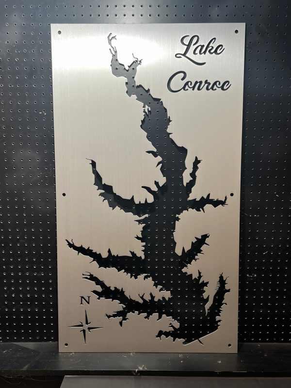 Lake Conroe map cutout on brushed metal with decorative script and compass rose, set against a perforated background.