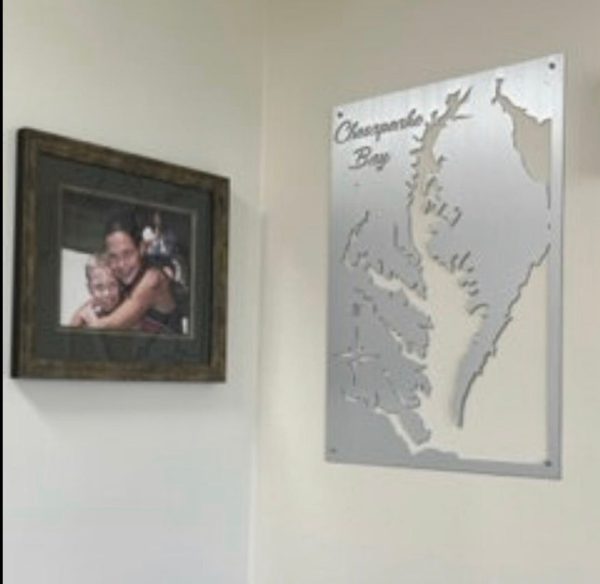 Framed family photo beside a custom metal map of Chesapeake Bay on a light-colored wall.