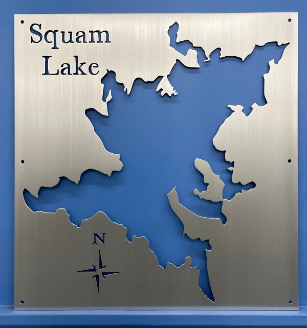 Squam Lake metal map with cutout design and compass rose, mounted on a blue wall.